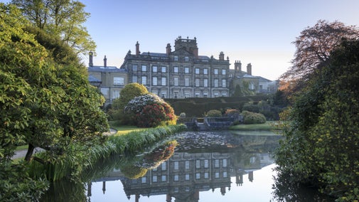 View of the house at Biddulph Grange from across a pond surrounded by trees and shrubs